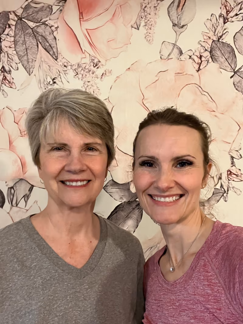 Laurie Howick, left, and her daughter Jayse, smiling in front of a pink floral wall