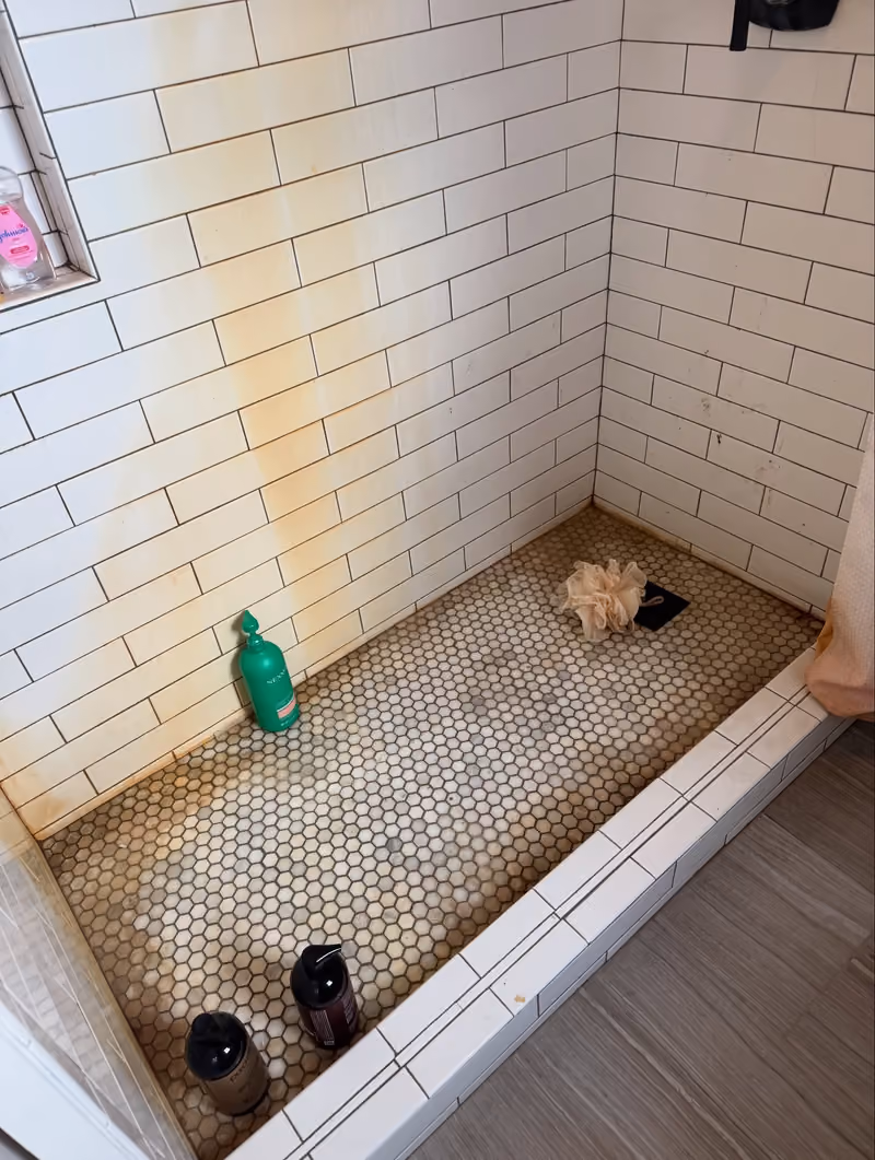 Before: white tile shower with rust stains running down the wall and dingy grout
